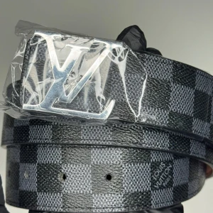 Louis Vuitton rutigt bälte med LV-spänne - Snyggt bälte från Louis Vuitton med klassiskt LV-spänne i silverfärg. Bältet har ett rutigt mönster i svart och grått och är tillverkat i skinn. Perfekt för dig som vill ha en exklusiv och trendig accessoar.