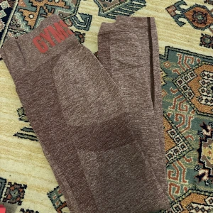 Bruna seamless leggings och set från Gymshark  - Bruna seamless leggings från Gymshark med hög midja och diskret mönster i tyget. Stretchigt material som sitter tight och bekvämt, perfekt för träning eller chill. Gymshark-logga i rött på linningen.
