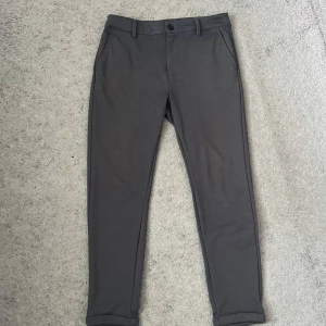 Grå comfort byxor i storlek S - Snygga grå kostymbyxor i klassisk modell med raka ben och diskreta fickor både fram och bak. Byxorna har bälteshällor och stängs med knapp och dragkedja. Perfekta för en stilren look och passar till många olika outfits.