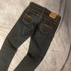 Mörkblå jeans från Nudie - Snygga mörkblå jeans från Nudie med klassiska orange sömmar och vågig brodyr på bakfickorna.  Modell Long John sitter slim fit. Skick 10/10 inga konstigheter. Ny pris 1600, mitt pris 499. Storlek 29/34