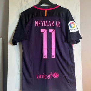 FC Barcelona Neymar Jr tröja M - Säljer en FC Barcelona matchtröja med Neymar Jr och nummer 11 på ryggen. Tröjan är mörklila med rosa detaljer, har korta ärmar och är tillverkad i Nike Dri-Fit material. På bröstet finns Qatar Airways, FIFA-märke och Barca-logga, samt La Liga-märke på ärmen.