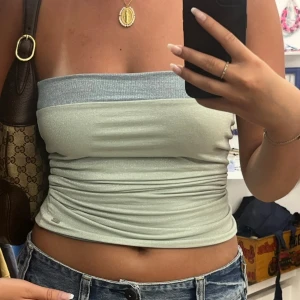 Glittrig blå bandeau tubtopp - Snygg glittrig bandeau tubtopp från Pull&Bear i ljusblått med en mörkare blå kant upptill. Toppen är axelbandslös och har en glansig finish som verkligen poppar. 