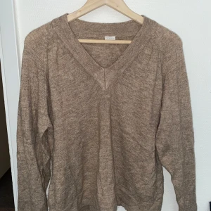 Beige stickad v-ringad tröja Stories - Mysig beige stickad tröja från & Other Stories med v-ringning och långa ärmar. Perfekt för lager-på-lager och chill höst- eller vinterstil. Skön passform och enkel att matcha med jeans eller kjol.