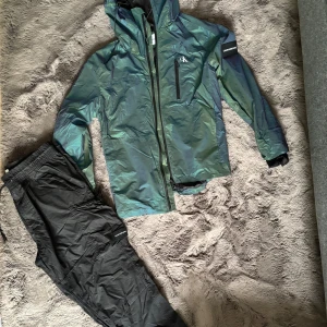 Grönsvart vindjacka från Calvin Klein Jeans - Snygg vindjacka från Calvin Klein Jeans i skimrande grönsvart färg. Jackan har huva, dragkedja framtill, bröstficka med dragkedja och logga på bröstet samt ärmen. Perfekt för dig som vill ha en stilren och modern look.