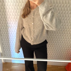 Grå kofta från Gina Tricot - Mysig grå kofta från Gina Tricot med rund halsringning och pärlemorknappar framtill. Storlek S, långa ärmar med lätt oversized passform. 14% ull & 7% alpackaull. 