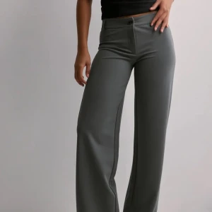 Grå wide kostymbyxor från Nelly -  grå kostymbyxor från Nelly med låg midja och vida ben. Byxorna har klassisk knapp och dragkedja framtill samt stilrena pressveck. Helt oanvända😍nypris 399