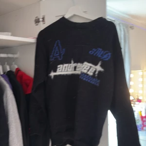 Svart stickad tröja med blått tryck - Svart stickad tröja med coola blå och vita detaljer samt tryck på bröstet. Långärmad modell med vit rand längs ärmen. Perfekt för dig som gillar streetstyle och vill ha något unikt i garderoben.