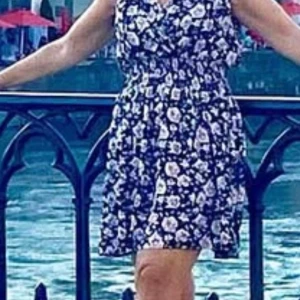 Blommig kortklänning med v-ringning - Söt kortklänning med blommigt mönster i rosa och vitt på marinblå botten. Klänningen har v-ringad omlottfront, resår i midjan och är ärmlös. Perfekt för varma dagar och har en luftig, flowy passform.