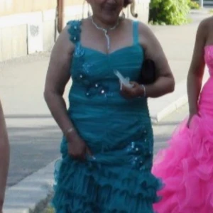 Turkos långklänning med volanger - Säljer en turkos långklänning med smala axelband och v-ringning. Klänningen har dekorativa paljetter upptill och massor av volanger nedtill som ger en riktigt festlig känsla. Perfekt för bal eller andra speciella tillfällen. Den är blå/grön 