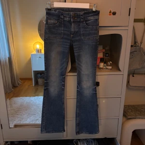 Blå bootcut jeans från H&M - Snygga blå bootcut jeans från H&M med låg midja. Jeansen har klassiska fickor fram och bak samt en lätt tvättad look. Perfekta för dig som gillar en retro vibe och vill ha ett par jeans med lite utsvängda ben.