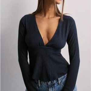 Mörkblå v-ringad långärmad topp - Snygg mörkblå topp med djup v-ringning och lång ärm. Toppen har en lätt utsvängd nederdel och är tillverkad i ett ribbat material som ger en cool struktur. Perfekt att styla med jeans för en trendig look.