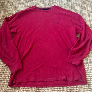 Röd långärmad tröja från Polo Ralph Lauren - Röd långärmad tröja från Polo Ralph Lauren i 100% bomull. Tröjan har en klassisk rund halsringning och blå broderad logga på bröstet. Materialet är mjukt och har en lätt strukturerad yta som ger en avslappnad vibe. Skriv gärna ifall frågor uppkommer eller om du vill se fler bilder, kolla gärna även in min profil ❣️