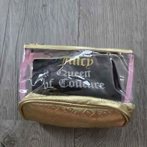 Juicy Couture necessärset i guld och svart - Necessärset från Juicy Couture med tre delar: en transparent necessär med guldiga detaljer och rosa kanter, en mindre guldig väska med präglat mönster och en svart tygväska med texten 'Queen of Couture' i strass. Perfekt för smink eller småprylar.