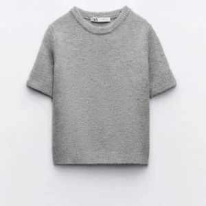 Grå stickad kortärmad tröja från Zara - Supermjuk grå stickad tröja från Zara med korta ärmar och rund hals. Perfekt för lager-på-lager och chill vibes. Ribbstickade kanter vid ärmslut och nederkant ger en clean look. Enkel att matcha med allt i garderoben. 