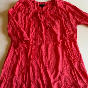 Korallrosa blus med knyt från Esmara - Säljer en korallrosa blus från Esmara med snygga broderade detaljer framtill och knytband vid halsen. Blusen har trekvartsärm med resår och är tillverkad i ett lätt och luftigt tyg, perfekt för varmare dagar.