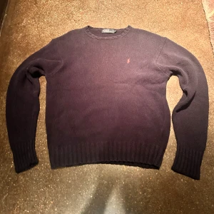Mörklblå stickad tröja Polo Ralph Lauren - Säljer en mörkblå stickad tröja från Polo Ralph Lauren. Klassisk rund halsringning, ribbade muddar och nederkant samt den ikoniska broderade loggan i rött på bröstet. Perfekt för dig som gillar stilren och tidlös design. Det står storlek M på etiketten, men passar som L.