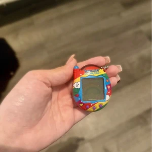 Tamagotchi Connection - Färgglad Tamagotchi Connection från Bandai. Virtuellt husdjur i regnbågsdesign med tre knappar och nyckelringsfäste. Skärmen är hel, inga synliga repor eller större slitage. Perfekt för samlare eller nostalgiker. Fungerar som den ska