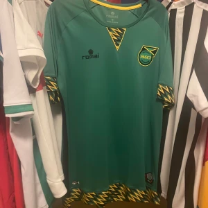 Jamaica fotbollströja Romai L Äkta - Jamaica landslagströja från Romai i grönt med gula och svarta blixtmönster på ärmslut och nederkant. .Mycket bra skick, Äkta