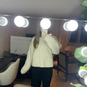 Oversized stickad vit tröja - Mysig oversized stickad tröja i vit färg med grovt kabelstickat mönster framtill och ribbade muddar. Tröjan har lång ärm och en avslappnad passform, perfekt för kalla dagar. Enkel att styla med både jeans och mjukisbyxor.