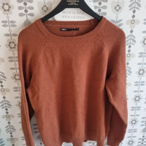 Rostbrun stickad tröja från Only - Mysig rostbrun stickad tröja från Only med rund halsringning och ribbade muddar. Perfekt för lager-på-lager under kyliga dagar. Enkel och stilren design som passar till det mesta.