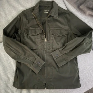 Mörkgrön overshirt  - Stilren mörkgrön overshirt från Selected Homme med två bröstfickor och dragkedja framtill. Klassisk krage och långa ärmar med knapp vid ärmslut. Perfekt för lager-på-lager och enkel att matcha till olika outfits. Modellen är 183 och väger 75 