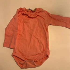 Rosa body med volang  - Rosa body med volang runt halsen. Storlek 74