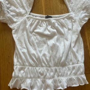 Vit topp från Primark XS - Supersöt vit topp från Primark i storlek XS. Toppen har puffiga kortärmar med broderade blommor och en smockad midja som ger en snygg siluett. Perfekt för varma dagar och har en fräsch, romantisk vibe.💓