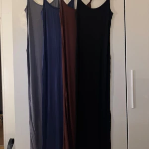Fyra långa bas-klänningar i olika färger - Fyra stilrena långklänningar med smala axelband i färgerna grå, blå, brun och svart. Modellen är rak och enkel, perfekt för att styla på olika sätt. Vill man ha enbart någon av klänningarna eller 2/3 så är det bara att höra av sig så löser vi det!