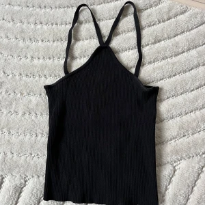 Svart ribbad linnetopp - En svart ribbad linnetopp med smala axelband och rak passform. Sparsamt använd 