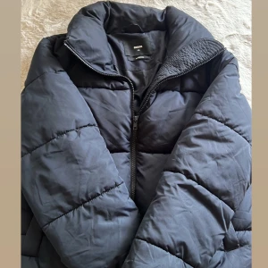 Svart pufferjacka från Bik Bok XS - Säljer en svart pufferjacka från Bik Bok i storlek XS. Jackan har hög krage, dragkedja framtill och är quiltad för extra värme. Perfekt för kyliga dagar och har en clean, stilren look.