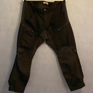 Svarta cargopants från Grant Outdoor - Svarta cargopants från Grant Outdoor med flera praktiska fickor och dragkedjor. Byxorna har en loose passform och är tillverkade i slitstarkt material, perfekta för utomhusaktiviteter. Snygg och funktionell design med detaljer som förstärkta knän och justerbara benslut.