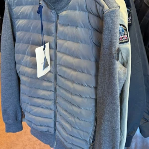 Grå cardigan från Moncler - Snygg grå dunväst från Moncler med quiltad framsida och dragkedja. Västen har en stilren look med ribbade muddar och Moncler-logga på ärmen. Tillverkad i bomull och polyester med dunfyllning för extra värme. Perfekt för lager-på-lager-stil.