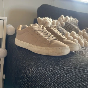 Beige sneakers från ZARA - Säljer ett par stilrena beige sneakers från ZARA med klassisk design. Skorna har snörning, platt vit sula och är tillverkade i syntetmaterial med en matt finish. Perfekta för dig som gillar en clean och enkel look till vardags.