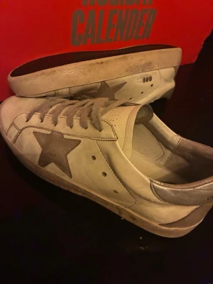 Vita sneakers från Golden Goose - Säljer ett par vita sneakers från Golden Goose med den ikoniska stjärnan på sidan och silverfärgade detaljer vid häl och snörning. Skorna har rund tå, snörning och platt sula. Perfekta för dig som gillar en avslappnad och trendig stil.