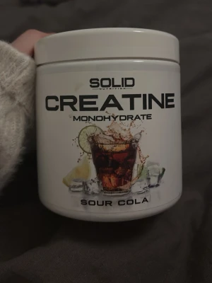 Kreatin Monohydrat Sour Cola - Burk med kreatin monohydrat från Solid Nutrition i smaken Sour Cola. Förpackningen är vit med svart text. Perfekt för dig som tränar och vill boosta din prestation. Har används ett enstaka gånger och är nästan helt full! 