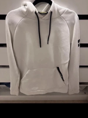 Vit hoodie med svart tryck - Snygg vit hoodie med svart dragsko och ett svart grafiskt tryck på ena ärmen. Hoodien har en stor ficka framtill med dragkedjedetalj. Tillverkad i mjukt material som känns skönt mot huden. Perfekt för en avslappnad streetwear-look.