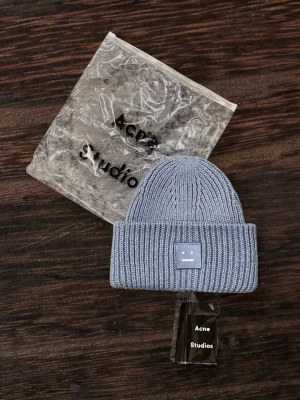 Ljusblå ribbstickad mössa Acne Studios - Snygg ljusblå ribbstickad mössa från Acne Studios med uppvikt kant och den klassiska Acne-loggan framtill. Tillverkad i mjukt och värmande material, perfekt för kyliga dagar. En stilren accessoar som lyfter din outfit.