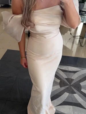 Champagnefärgad långklänning offshoulder - Elegant långklänning i champagnefärg med offshoulder och puffiga ärmar. Klänningen har en figurnära passform, slits bak. Endast använd en gång. Köpt för 2500. Perfekt till bröllop, bal, dop, gala, fest eller andra event.