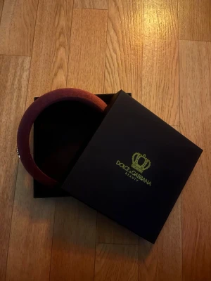 Vinrött sammetsdiadem Dolce & Gabbana - Säljer ett vinrött aldrig andvänts, vadderat diadem från Dolce & Gabbana i mjuk sammet. Diademet har en liten guldfärgad krona som detalj på sidan och kommer i originalask. Perfekt accessoar för att lyfta din look.