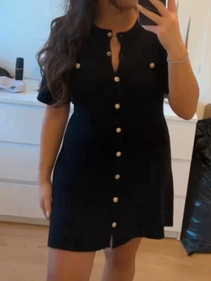 Svart kortklänning med guldknappar - Använd en gång. Tvättad. Köpt i H&M. Storlek M.