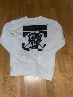 Vit sweatshirt från Off-White - Säljer en clean vit sweatshirt från Off-White med svart grafiskt tryck på ryggen och liten logga framtill. Tröjan har rund hals, långa ärmar och är gjord i mjuk bomull. Perfekt för dig som gillar streetwear och vill sticka ut lite extra.