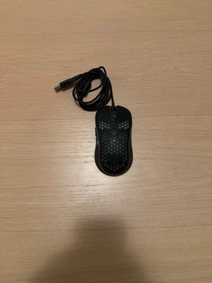 SR7 Gaming Mouse - SR7 Gaming Mouse med lättviktsdesign och honeycomb-mönster för optimal ventilation. Utrustad med sidoknappar och justerbar DPI. Kabelansluten för låg latens. Musen är i nytt skick utan synligt slitage, perfekt för gaming och precisionsarbete.