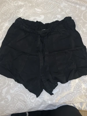 Svarta shorts med snörning från H&M - Säljer ett par svarta shorts från H&M i storlek 36. De har hög midja med resår och snörning framtill i linne material. Aldrig använts. 