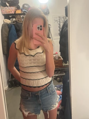 Stickad ärmlös topp med svarta detaljer - Supersöt stickad topp i offwhite med svarta vågiga detaljer längs kanterna. Toppen är ärmlös och croppad med ett luftigt, mönstrat stickat material som ger en somrig vibe. Nästan helt oanvänt och säljer pga att det är för litet❤️