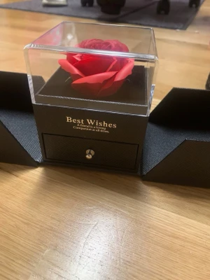 Smyckesask med röd ros och låda - Snygg svart smyckesask med en konstgjord röd ros i genomskinligt lock. Asken har en utdragbar låda för smycken och texten 'Best Wishes' på framsidan. Perfekt för att förvara ringar, halsband eller örhängen.