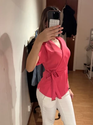 Rosa omlottopp med knyt i midjan - Knallrosa omlottopp med kort ärm och knyt i sidan. Storlek S, men passar även xs. Använd en gång, som ny! Köpte den utomlands. 