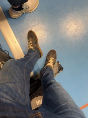 Bruna margiela gats med beige detaljer - Säljer ett par mörkgrå sneakers med beige snörning och sula. Skorna har en klassisk låg profil och är tillverkade i mocka och skinn, vilket ger en snygg kontrast mellan material och färg. Perfekta för dig som gillar stilrena och tidlösa sneakers.