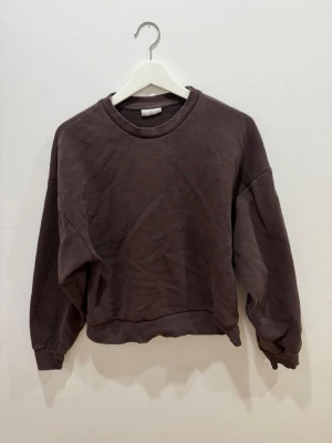 Brun sweatshirt från Gina Tricot - Mysig brun sweatshirt från Gina Tricot, basically basics-kollektionen. Tröjan har rund halsringning, ribbade muddar vid ärmslut och nederkant samt en avslappnad passform. Perfekt för en chill och enkel stil.