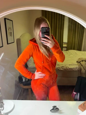 Orange velour loungewear-set - Mysigt loungewear-set i orange velour med hoodie och matchande byxor. Hoodien har dragkedja och fickor, byxorna har resår i midjan och bakfickor med knapp. Perfekt för chill dagar hemma eller när du vill vara extra comfy.