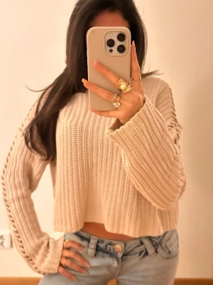 Beige stickad tröja - Trendig beige stickad tröja med croppad passform och vida ärmar. Tröjan har ett grovt ribbstickat mönster och dekorativa håldetaljer längs ärmarna. Perfekt att styla med jeans för en avslappnad look.